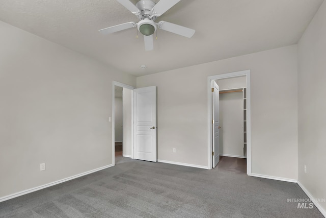 unfurnished bedroom with carpet, baseboards, a walk in closet, and ceiling fan
