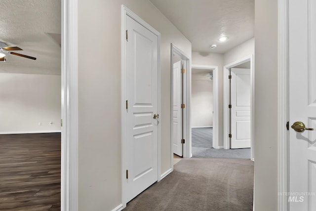 hallway featuring baseboards, carpet flooring, and a textured ceiling