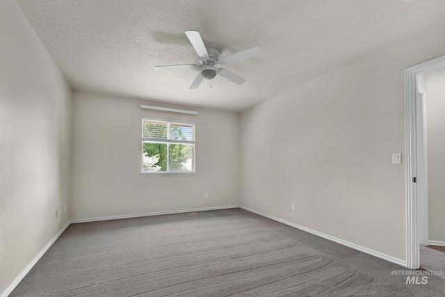 empty room with dark carpet, ceiling fan, baseboards, and a textured ceiling
