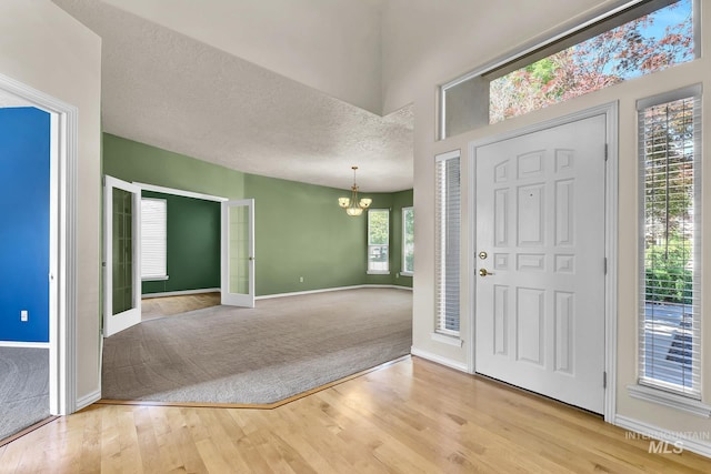 carpeted entrance foyer with a chandelier, wood finished floors, baseboards, and a textured ceiling