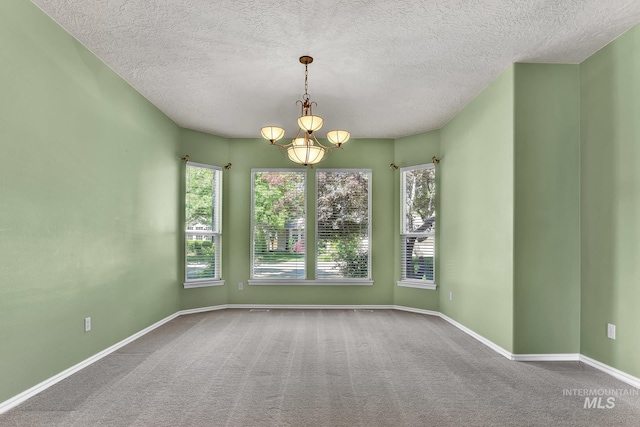 carpeted empty room featuring a chandelier, a textured ceiling, and baseboards