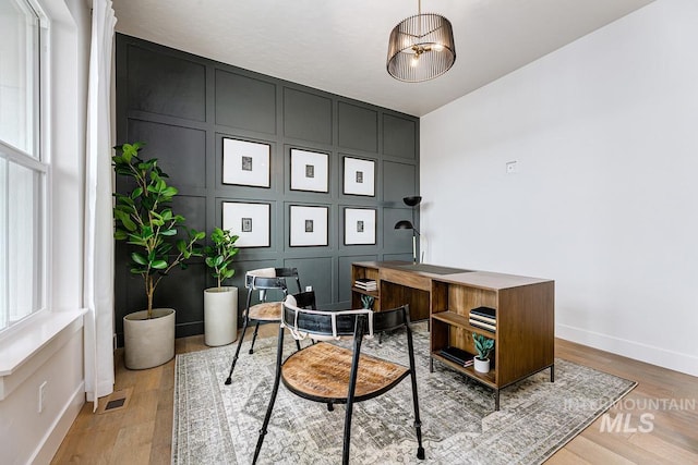 office area with baseboards, wood finished floors, visible vents, and a decorative wall