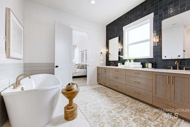 bathroom with double vanity, a freestanding bath, and a sink