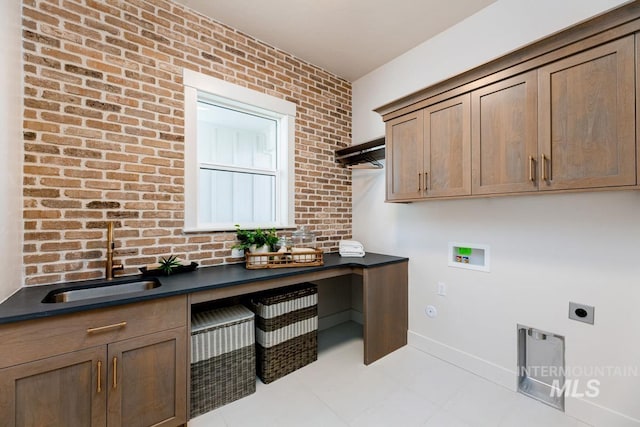 washroom featuring cabinet space, a sink, electric dryer hookup, and brick wall