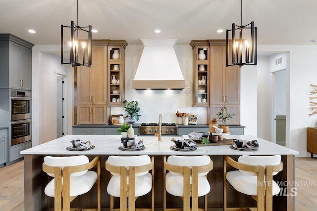 kitchen featuring light stone counters, tasteful backsplash, custom range hood, glass insert cabinets, and stainless steel double oven