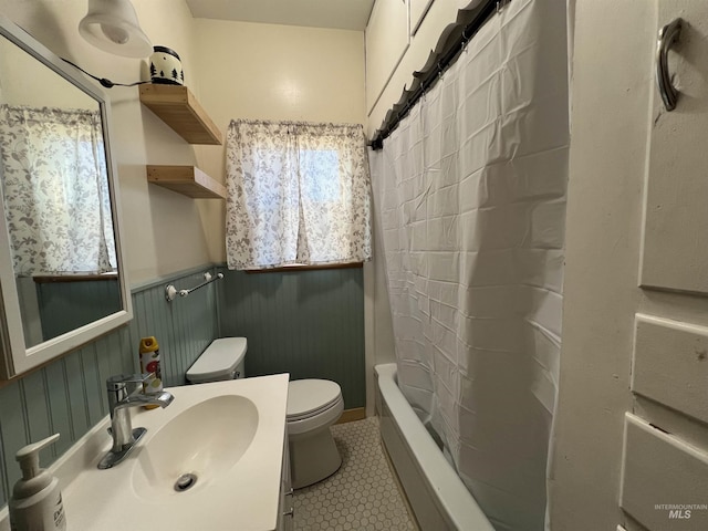 full bath featuring toilet, a wainscoted wall, a sink, tile patterned floors, and shower / tub combo with curtain