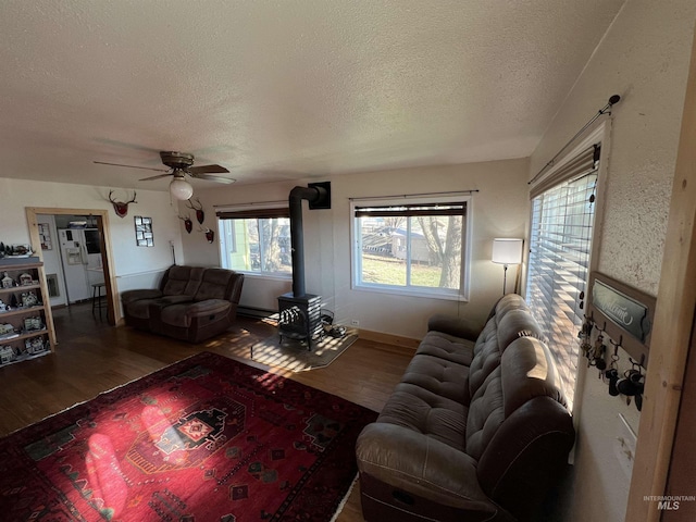 living room with a wood stove, ceiling fan, a textured ceiling, and wood finished floors