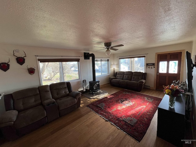 living area with a wood stove, ceiling fan, a textured ceiling, wood finished floors, and baseboards