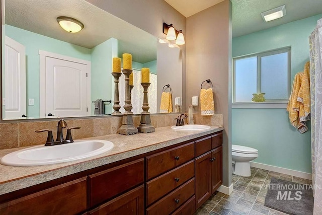 bathroom featuring double vanity, baseboards, toilet, and a sink