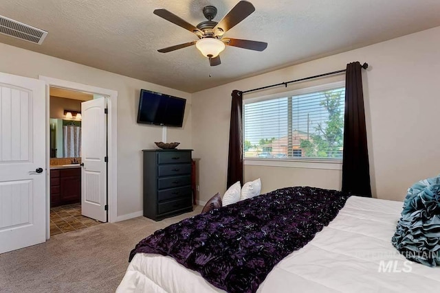 carpeted bedroom featuring baseboards, visible vents, a ceiling fan, ensuite bathroom, and a textured ceiling