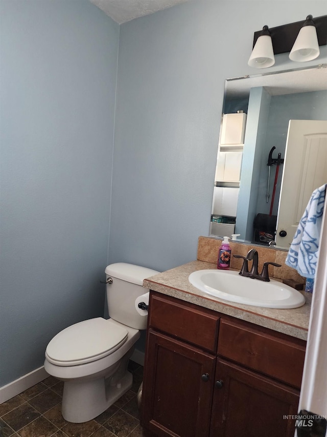 half bath with toilet, baseboards, and vanity