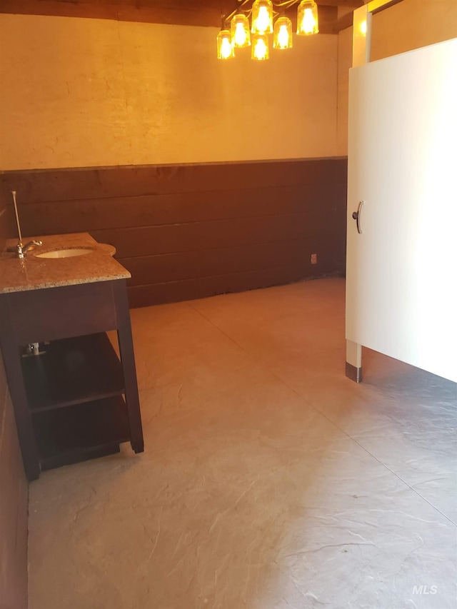 kitchen featuring light stone counters, a wainscoted wall, concrete flooring, and wooden walls