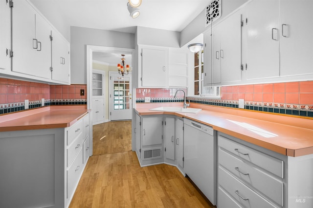 kitchen featuring light wood-type flooring, a sink, white cabinets, white dishwasher, and decorative backsplash