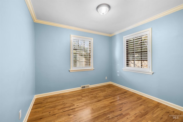 spare room with visible vents, wood finished floors, baseboards, and ornamental molding