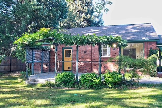 view of front facade featuring a front yard, fence, brick siding, and roof with shingles