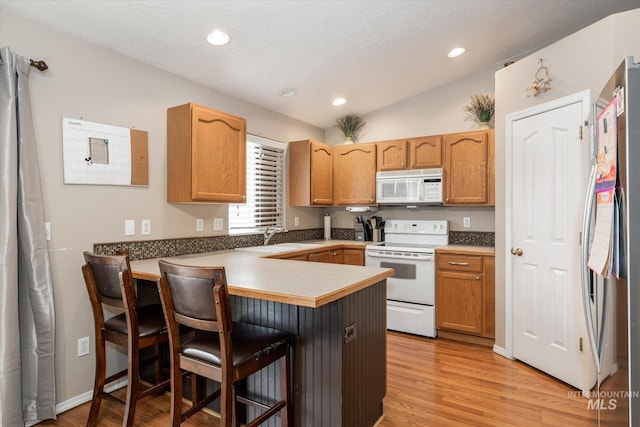 kitchen with vaulted ceiling, a breakfast bar, kitchen peninsula, white appliances, and light hardwood / wood-style flooring