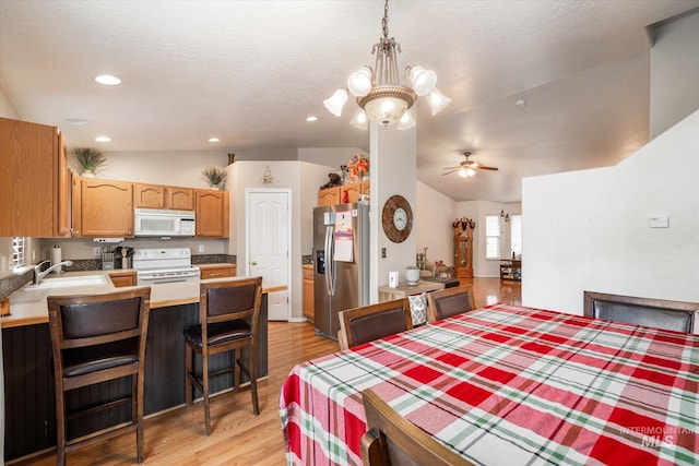 dining area with sink, ceiling fan, a textured ceiling, vaulted ceiling, and light wood-type flooring