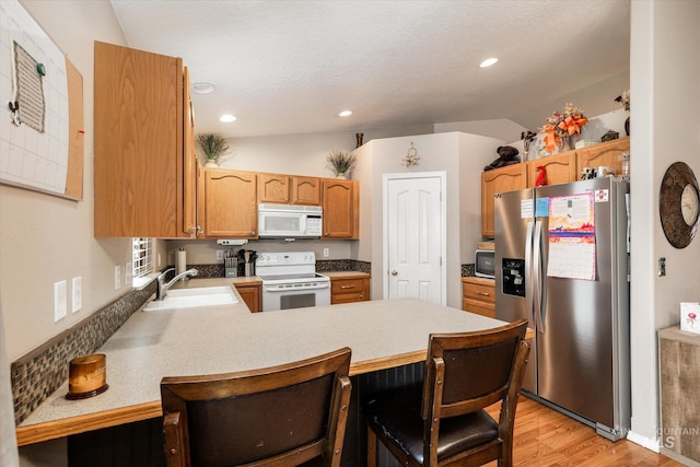 kitchen featuring lofted ceiling, sink, white appliances, a kitchen breakfast bar, and kitchen peninsula