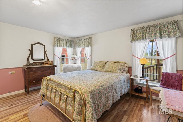 bedroom with baseboards, multiple windows, and wood finished floors