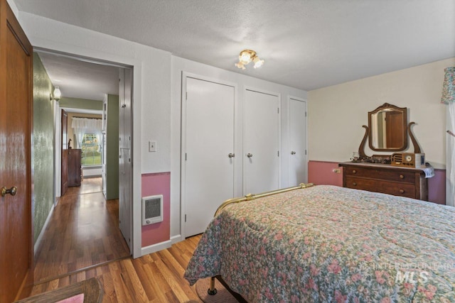 bedroom featuring two closets, baseboard heating, heating unit, and wood finished floors