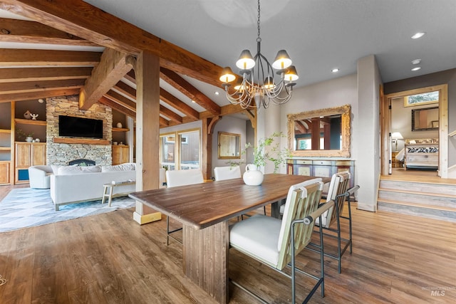 dining room featuring built in features, hardwood / wood-style flooring, a fireplace, vaulted ceiling with beams, and an inviting chandelier