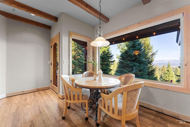 dining area with hardwood / wood-style flooring, a wealth of natural light, a mountain view, and beamed ceiling