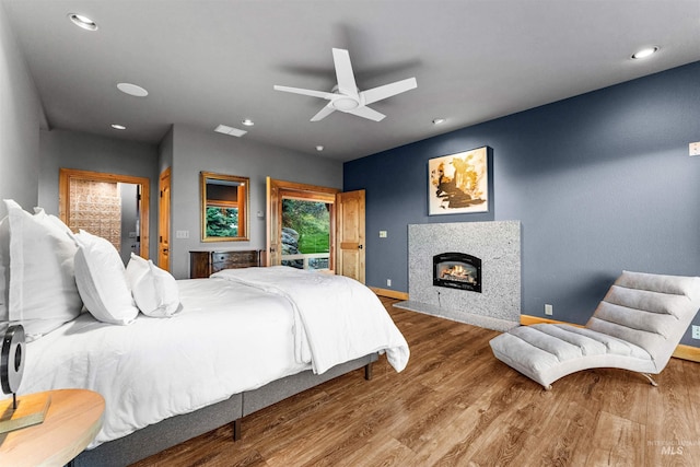 bedroom with a tiled fireplace, hardwood / wood-style floors, and ceiling fan