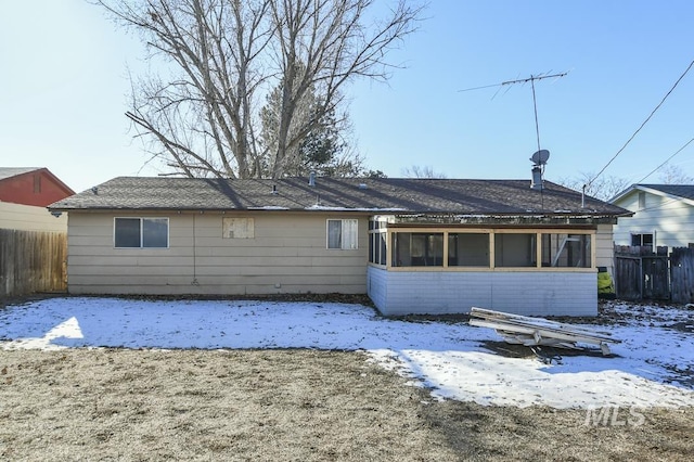 snow covered rear of property featuring a sunroom