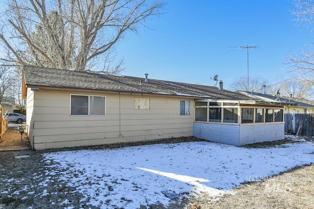 snow covered rear of property featuring a sunroom