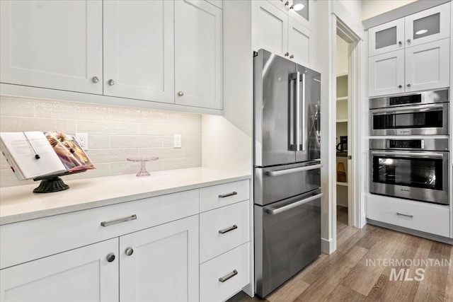 7478 W Palamas, Eagle, ID 83616 - kitchen featuring stainless steel appliances, light countertops, light wood-type flooring, white cabinets, and decorative backsplash