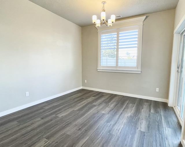 spare room with dark wood-style flooring, an inviting chandelier, and baseboards