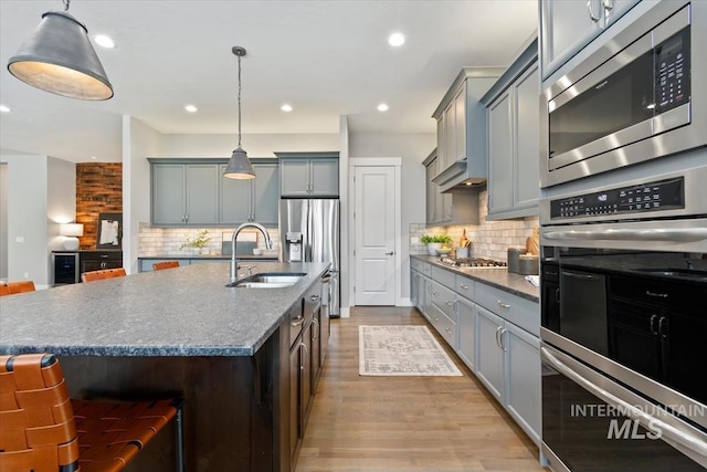 kitchen with decorative backsplash, an island with sink, light wood-style flooring, appliances with stainless steel finishes, and a sink