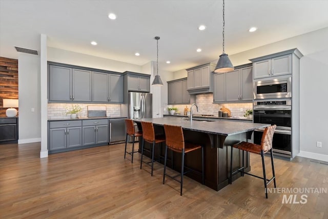 kitchen with gray cabinetry, stainless steel appliances, dark wood-type flooring, a sink, and a kitchen breakfast bar