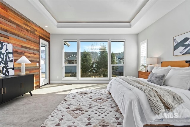 carpeted bedroom with an accent wall, a tray ceiling, and wood walls