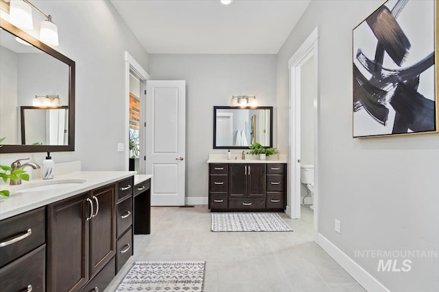 full bathroom with two vanities, a sink, toilet, and baseboards