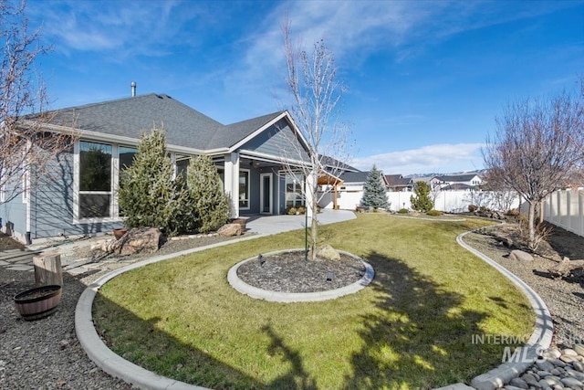 rear view of property with a yard, a fenced backyard, a patio, and a shingled roof