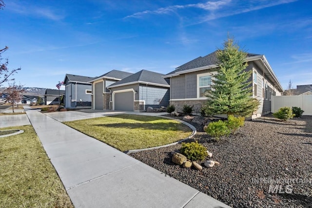 view of front of property with a garage, fence, stone siding, concrete driveway, and a front yard