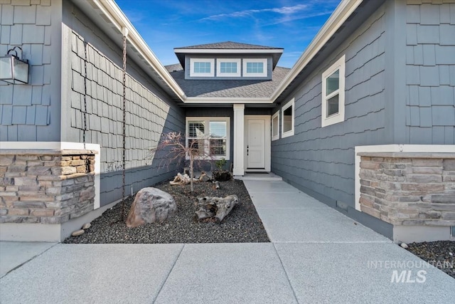 view of exterior entry featuring stone siding and a shingled roof