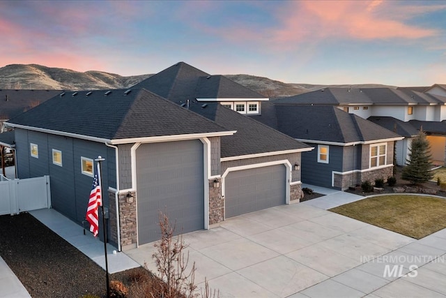 view of front of property with a garage, stone siding, fence, and a mountain view