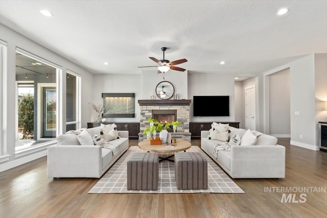 living area featuring baseboards, a stone fireplace, wood finished floors, and recessed lighting