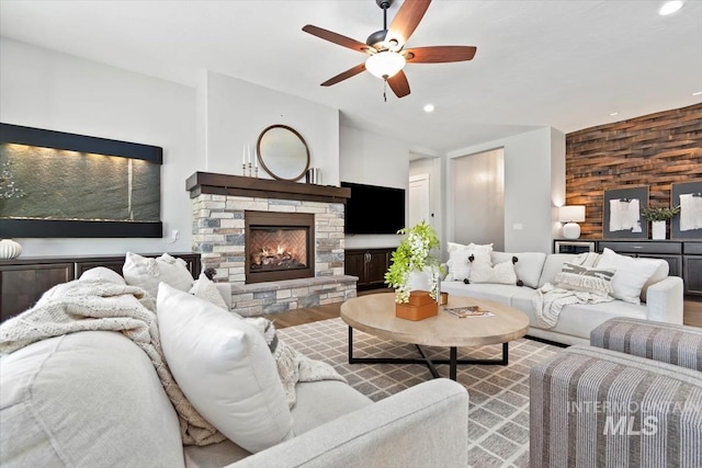 living room with recessed lighting, ceiling fan, wooden walls, a stone fireplace, and wood finished floors