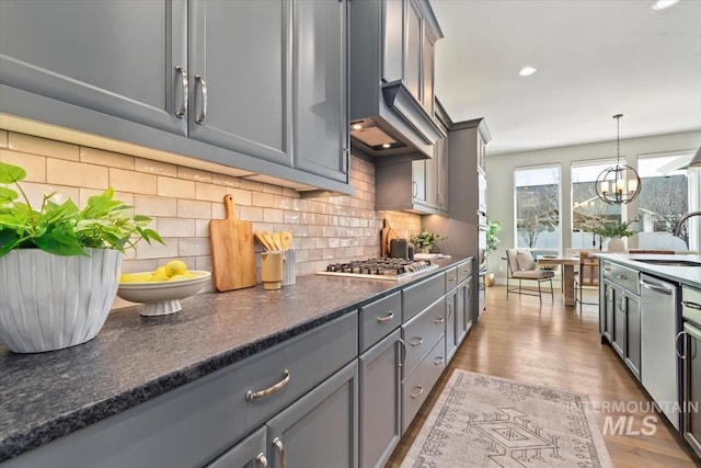 kitchen featuring wood finished floors, gray cabinets, stainless steel appliances, a chandelier, and backsplash