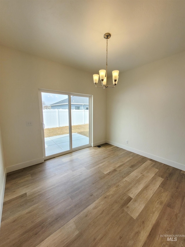 empty room with wood-type flooring and an inviting chandelier