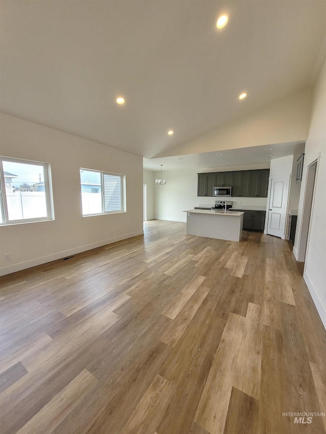 unfurnished living room featuring light hardwood / wood-style floors, lofted ceiling, and a notable chandelier