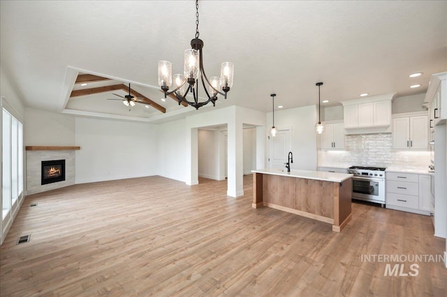 kitchen with white cabinets, open floor plan, light countertops, high end range, and a center island with sink