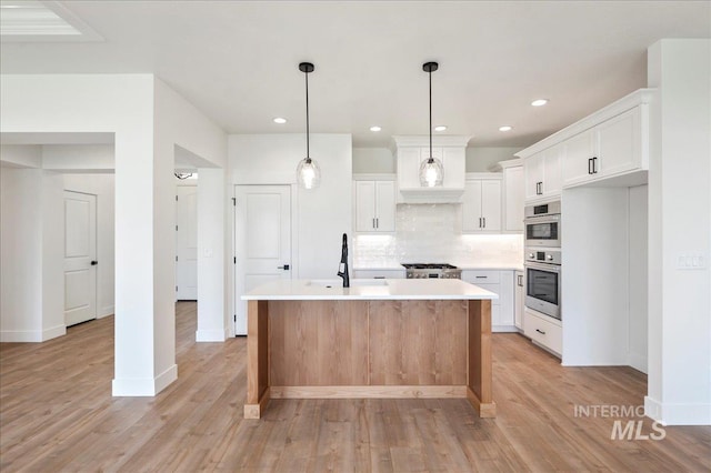 kitchen with tasteful backsplash, light countertops, a kitchen island with sink, white cabinets, and a sink