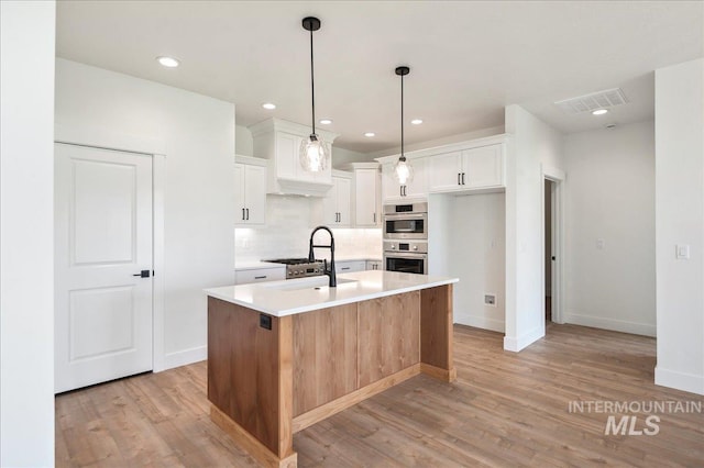 kitchen with a center island with sink, light countertops, white cabinets, a sink, and light wood-type flooring