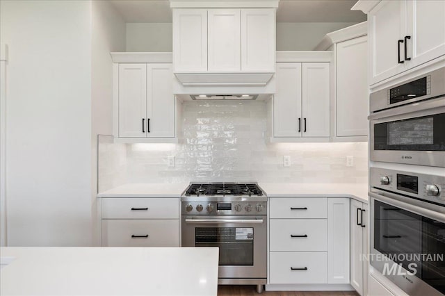 kitchen featuring white cabinetry, light countertops, appliances with stainless steel finishes, decorative backsplash, and custom range hood