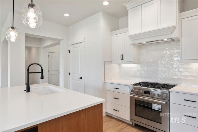 kitchen featuring stainless steel gas range oven, a sink, white cabinets, light countertops, and pendant lighting