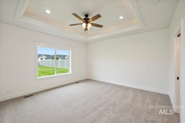 empty room with carpet, visible vents, a tray ceiling, and crown molding